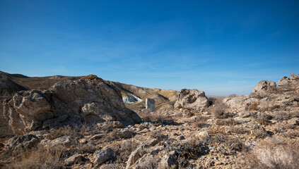A rugged desert landscape stretches across rolling hills, with a striking isolated rock formation...