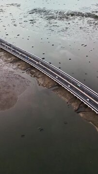 Aerial view of Bali Mandara Toll road bridge cutting across mangrove forest and low tide mud reveals tropical scenery as the modern highway floats above natural wetlands and coastal landscape