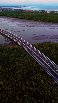 From above Bali Mandara Toll road stretches like a ribbon over mangrove forest and tidal mud during low tide while tropical landscape frames the modern bridge in striking drone perspective