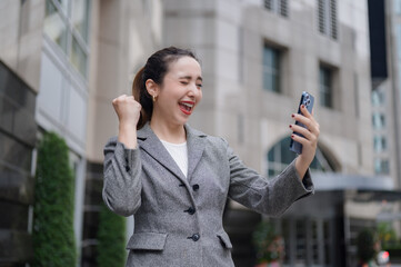 Fototapeta premium Excited businesswoman celebrating success while using smartphone outdoors.