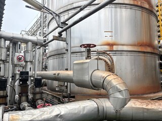 Naklejka premium This photo shows a large, weathered industrial storage tank with multiple pipes and valves connected to it, conveying a sense of heavy industry and complex processing within a factory or plant.