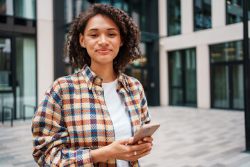A smiling woman happily using her phone in a vibrant urban setting, radiating positivity and joy