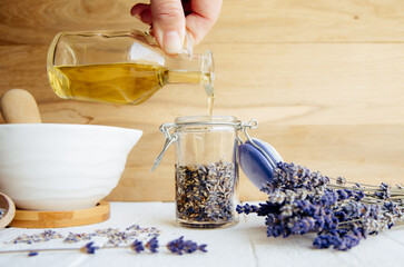A woman makes cold-infused lavender olive oil. She pours olive oil over dried lavender blossoms in...