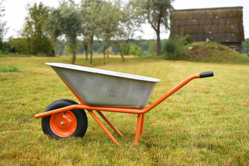 Wheelbarrow resting on green grass near wooden barn in countryside