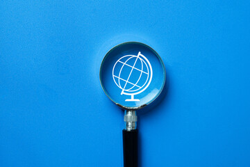 A magnifying glass over a globe icon. A concept for global business, international market research, analyzing worldwide trends, and globalization strategy. For economics and finance.