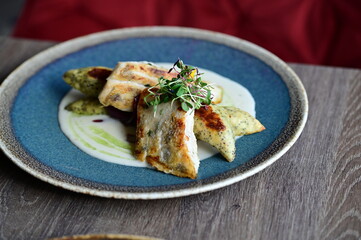 Close-up of a grilled fish fillet served with creamy white sauce and fresh herbs on a plate.