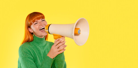 Cheerful young woman with orange hair using a megaphone against a bright yellow background during a lively event in a vibrant studio setting
