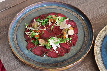Close-up view of beef carpaccio with parmesan, served on a rustic plate in a restaurant setting,...