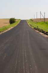 black new asphalt on the highway against the background of the blue sky, a newly built asphalt highway made of bitumen with crushed stone and sand in the countryside