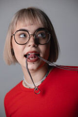 Young caucasian female with short blond hair and glasses biting chain, studio