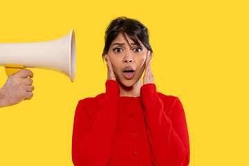 Woman covers ears in surprise as loudspeaker is directed towards her against a bright yellow background