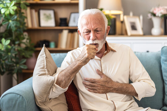 Senior, sick man and couch with chest pain on sofa for cardiac arrest or bronchitis at home. Elderly, male person or patient with illness, virus or viral infection for lung disease or heart attack.