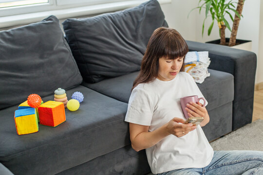 Young mother using phone with coffee at home - Powered by Adobe