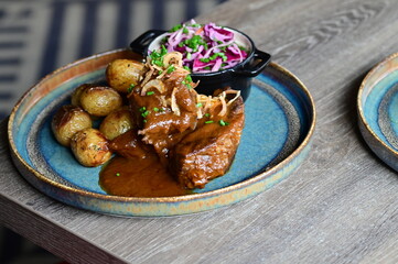 Beef rib served with roasted potatoes and cabbage salad, traditional European cuisine, hearty homemade meal on a plate.