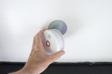 Homeowner seen installing a new generation smoke detector to the ceiling of an old, Grade 2 listed...