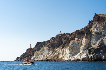 Fototapeta premium Sailboat Cruising by Rugged Volcanic Cliffs with Lighthouse