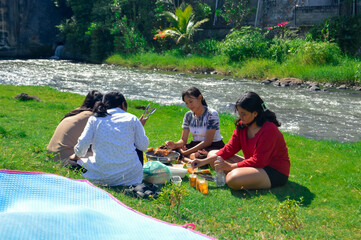Sitting near the river, four girls wait quietly as skewered sausages and chicken cook on the...
