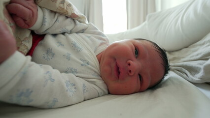 Newborn baby gesturing and moving under a blanket, grimacing with a curious expression, highlighting the early movements and expressions typical in the first month of life