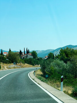 Curved road leading to village houses with scenic landscape under clear blue sky in Grebastica, Croatia.