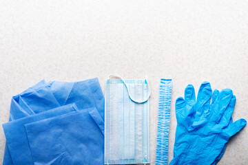 Healthcare background of disposable face mask, gloves, hat and scrubs laying on table flat lay view