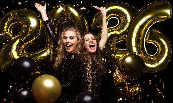 Happy gorgeous girls in stylish sexy party dresses holding gold 2026 balloons, having fun at New Year's Eve Party.