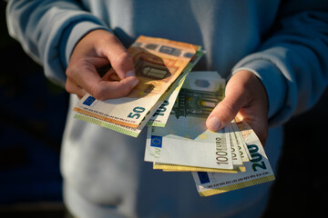 Person holding euro banknotes in hands, counting money outdoors. Close-up view of 50, 100, and 200 euro bills