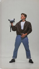 Man in leather jacket holding vintage camcorder with confident pose. Concept of retro media,...