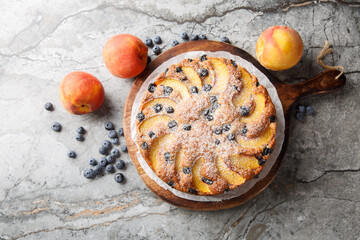Homemade pie with fresh peaches and blueberries close-up on a wooden board on the table. horizontal top view from above