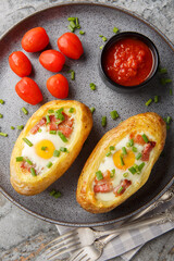 Baked potato in jacket loaded with bacon and egg closeup on the plate on the table. Vertical top view from above