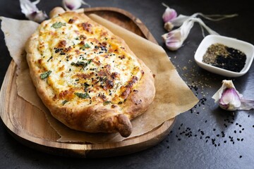 Freshly baked Georgian khachapuri bread filled with cheese and herbs, served on parchment paper over a rustic wooden board. Traditional Georgian cuisine, homemade comfort food.