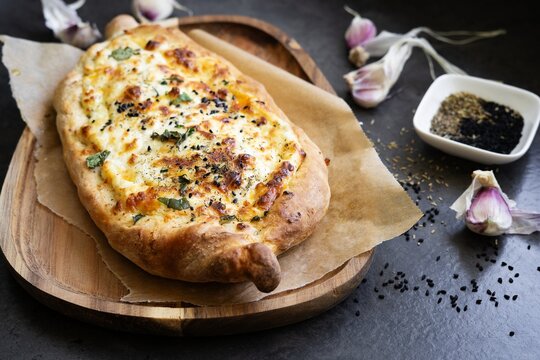 Freshly baked Georgian khachapuri bread filled with cheese and herbs, served on parchment paper over a rustic wooden board. Traditional Georgian cuisine, homemade comfort food.