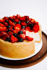 Fresh fruit cheesecake topped with strawberries and blueberries on a white background