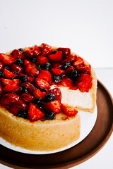 Delicious cheesecake topped with fresh strawberries and blueberries on a wooden platter