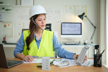 Young architect woman reviewing project plans and building mock ups in office.
