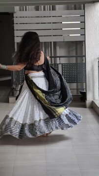 Woman in black and white lehenga with golden lagdi patta border dupatta twirling gracefully while playing garba, showcasing modern Navratri fashion for Garba and festive tradition.