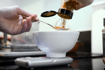 Chef's hand pours orange spices into cup on kitchen scale placed on kitchen counter.
