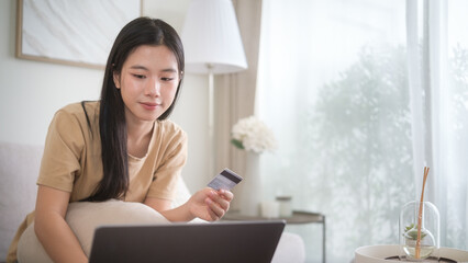 Smiling young woman shopping online with laptop and credit card at home.
