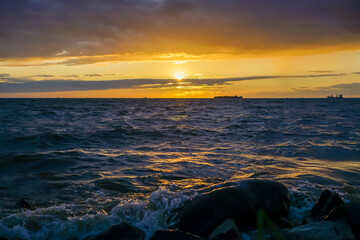 Naklejka premium Golden Sunset over the Ocean with Rocks in the Foreground