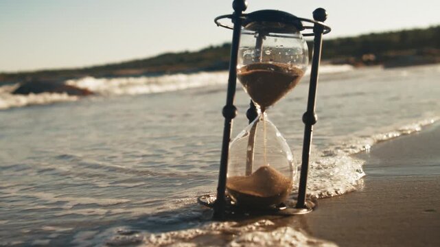 Golden Hour Light Reflects Through Transparent Hourglass As Tide Creeps In, Marking The Flow Of Time And Beauty Of The Moment. Countdown Scene In Coastal Atmosphere.