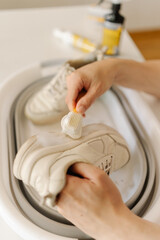 Close-up hands of unrecognizable man cleaning white sneaker with brush and cleaning foam, restoring...