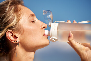 Young woman staying hydrated by drinking water from a clear bottle outdoors