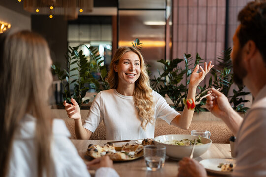 Friends enjoying pizza and salad, talking and gesturing in restaurant