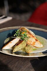 Close-up of a grilled fish fillet served with creamy white sauce and fresh herbs on a plate.
