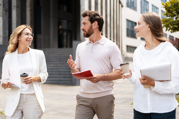 Businesspeople walking and talking in the city holding coffee and documents