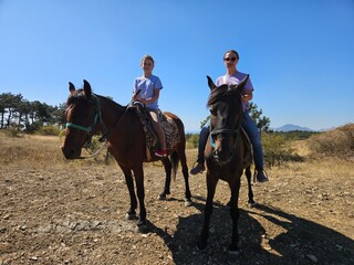 Mother and daughter enjoy a sunny horseback ride in the mountains. Ideal for family vacation, travel blogs, and articles about outdoor adventures or active lifestyles.