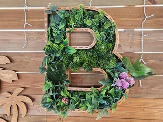 Creative wooden letter 'B' filled with faux succulents and green plants. Rustic eco-decor for events, interiors, or personalized branding on a wooden background.