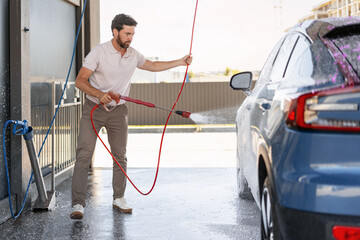 Man washing his blue car with soap and high pressure water jet