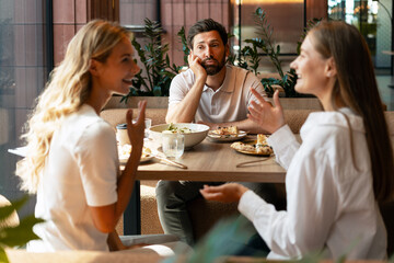 Bored man listening to two women chatting during lunch