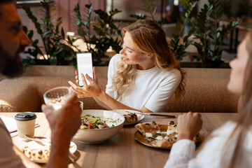 Businesswoman showing smartphone screen during business lunch with colleagues