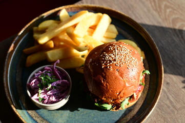 Juicy burger served with golden French fries on a plate in a restaurant setting. A classic and appetizing meal, perfect representation of comfort food and casual dining.